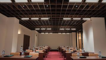 Un salón de conferencias con filas de mesas, sillas y botellas de agua.