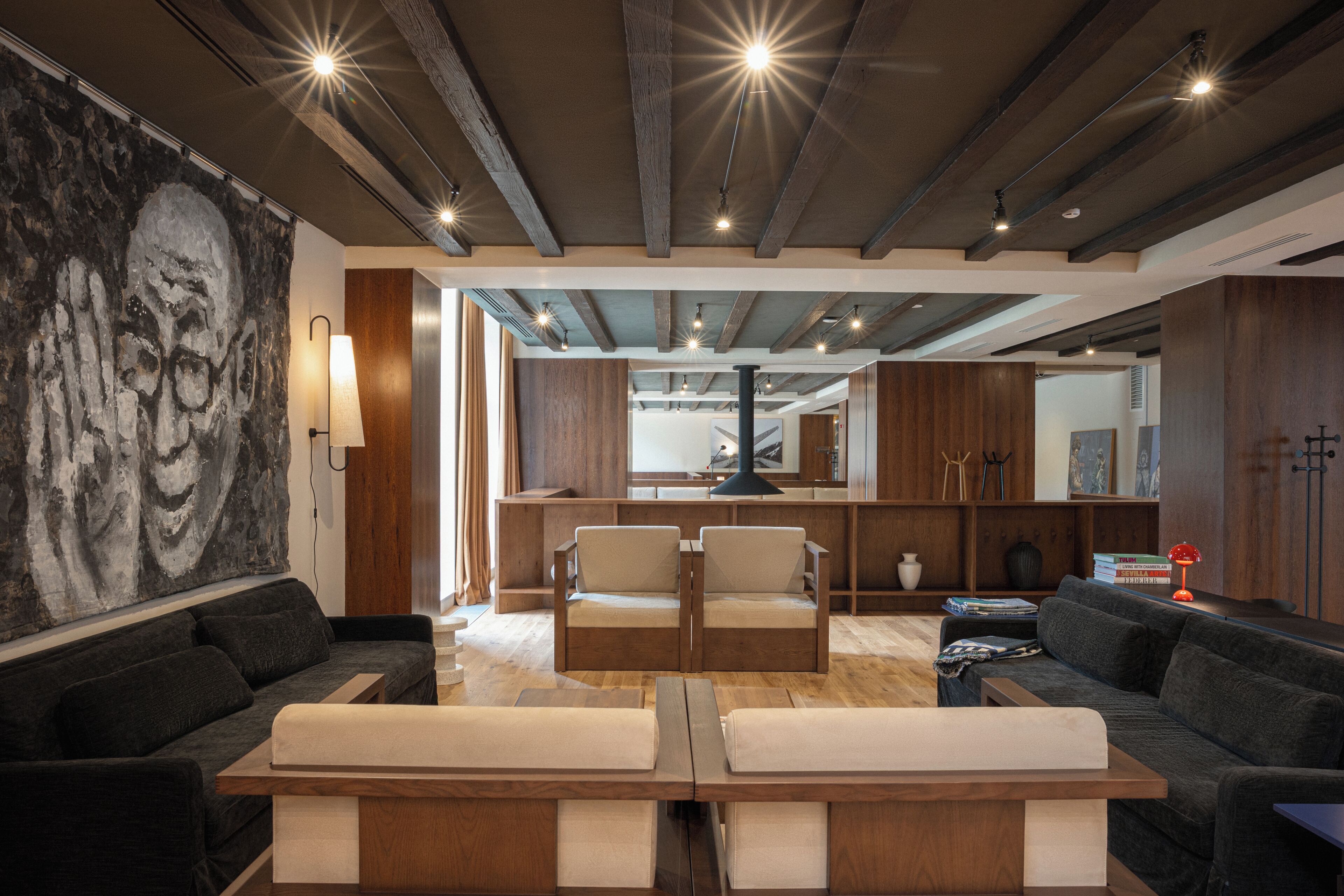 Una sala de estar moderna con un cuadro abstracto grande, muebles de madera y un techo alto con vigas a la vista.