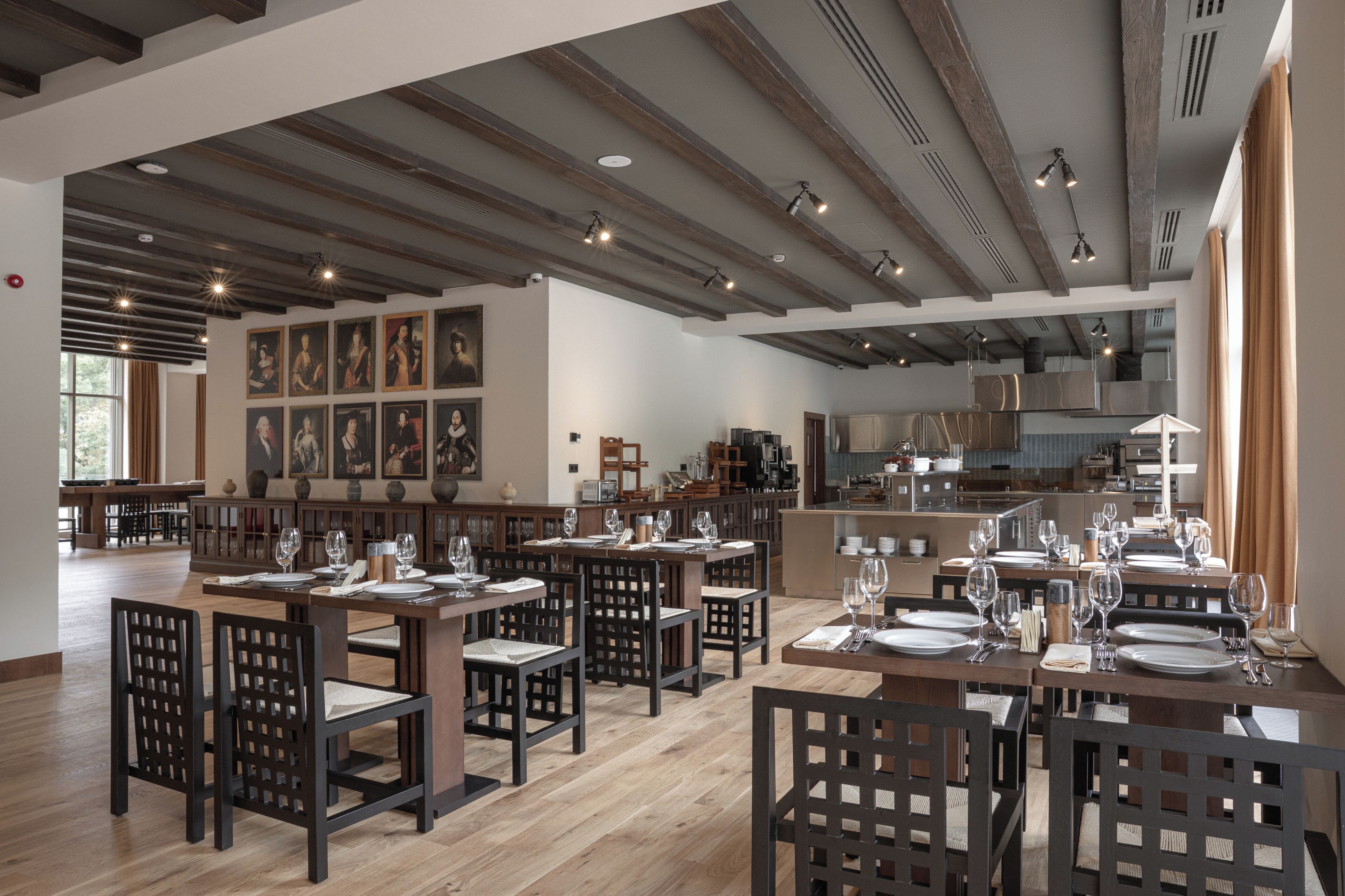 Un restaurante con mesas y sillas de madera, una zona de cocina y obras de arte en las paredes.