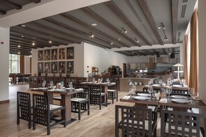 Un restaurante con mesas y sillas de madera, una zona de cocina y obras de arte en las paredes.