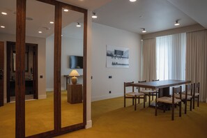 Habitación de hotel con zona de comedor, un espejo grande, televisor y un cuadro en la pared.