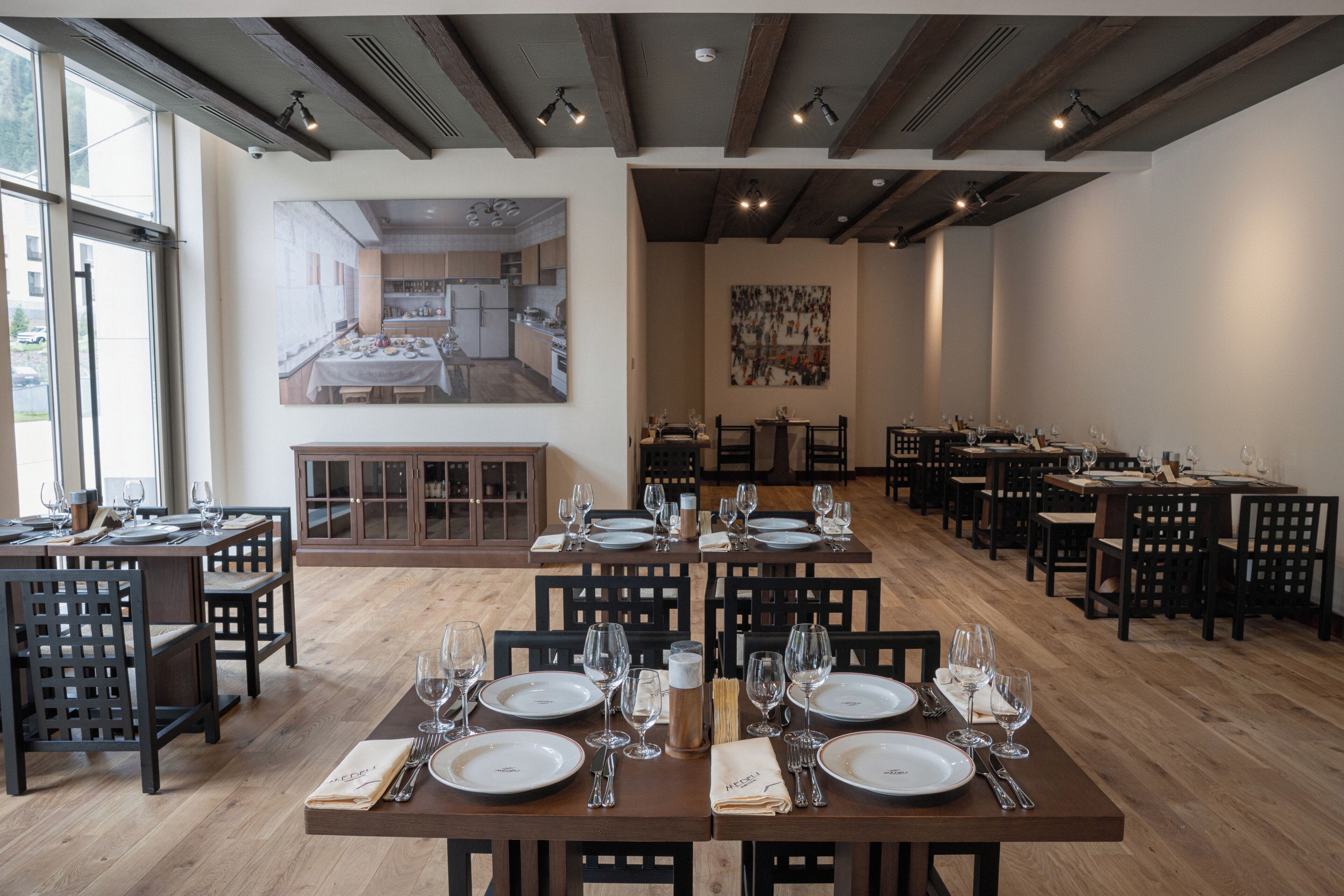 Un restaurant doté de nombreuses tables, d’un sol en bois et d’un grand tableau accroché au mur.