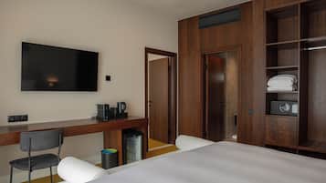 A hotel room with a bed, a desk with a chair, a television, a wardrobe, and a small kitchenette.