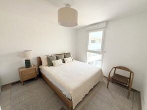 Een slaapkamer met een bed, nachtkastje, lamp, stoel en raam.