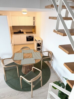Een compacte keuken met moderne apparaten, een eethoek met een ronde tafel en stoelen, en een houten trap.