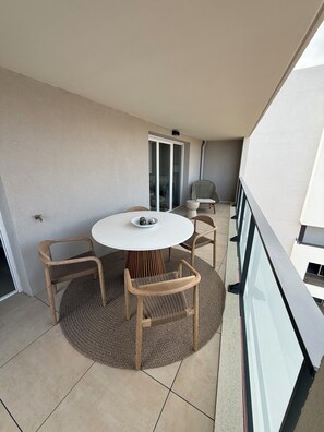 Een balkon met een ronde tafel en vier stoelen, een glazen deur en uitzicht op een gebouw.