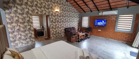 A hotel room with a bed, a seating area with a table, a television, and a brick wall.