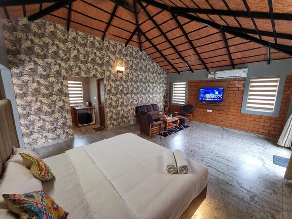 A hotel room with a bed, a seating area with a table, a television, and a brick wall. - KK SELFIE POINT RESORT (Coimbatore)