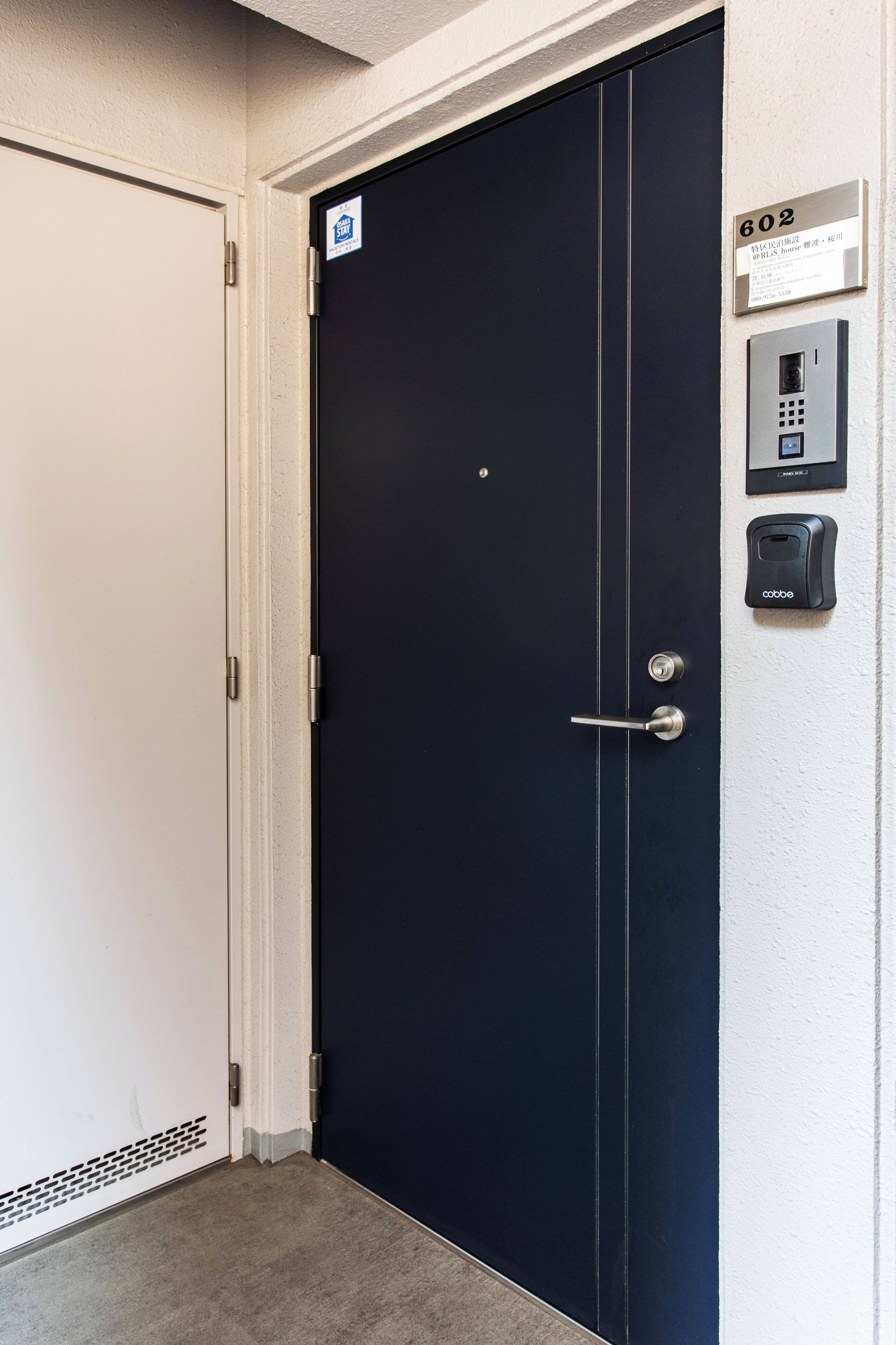 A black door with a keypad lock, a 'Stay' sign, and a number plate on the wall.