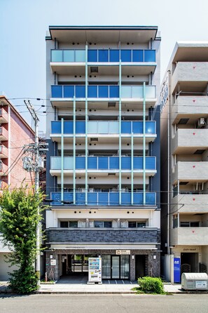 Un immeuble à plusieurs étages doté d’une façade plate, de plusieurs balcons et d’une entrée au niveau du sol, reconnaissable à une enseigne.
