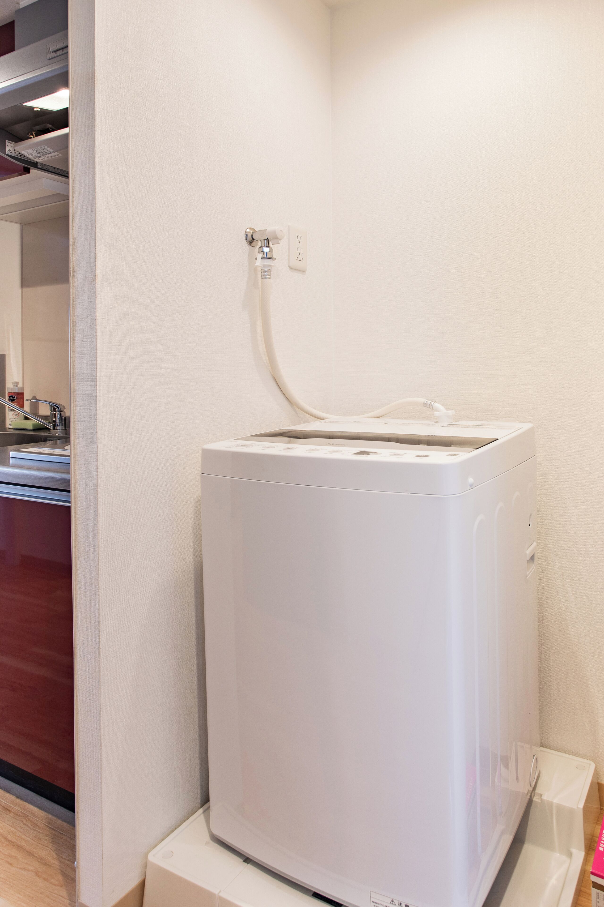 A white appliance, possibly a washer, on a white base unit, with a power outlet above it on the wall.