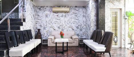 Un vestíbulo con pared de mármol, un sofá, sillas, una mesa pequeña con un florero y una escalera.