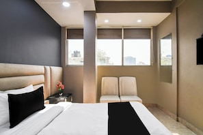 A hotel room with a bed, two chairs, a nightstand, a vase with flowers, a window with a view, and a flat-screen TV.