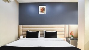 Une chambre d’hôtel avec un grand lit, une tête de lit, une table de chevet avec une lampe et un tableau encadré au mur.