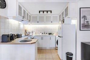 A compact kitchen with white cabinets, a stove, a sink, and a refrigerator. - Modern Apartment with Free Parking | Wi-Fi | Netflix | 5km to CBD & Glenelg (Plympton)