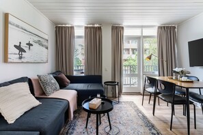 A modern living room with a sofa, a coffee table, a dining table with chairs, and a view through the glass doors. - Modern Apartment with Free Parking | Wi-Fi | Netflix | 5km to CBD & Glenelg (Plympton)