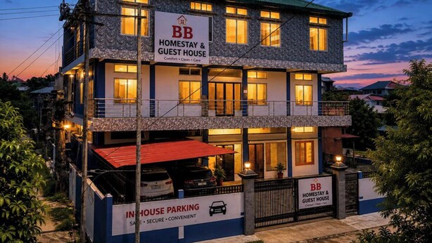A two-story building with a sign indicating it is a homestay and guest house, featuring a parking area with a red roof. - B.B.Homestay & Guest House (Tezpur)