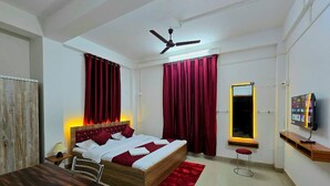 A bedroom with a bed, a desk, a chair, a TV, a ceiling fan, and a window with curtains.