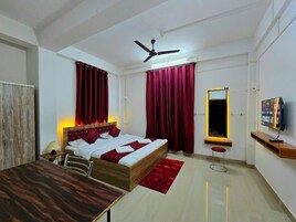 A bedroom with a bed, a desk, a chair, a TV, a ceiling fan, and a window with curtains.