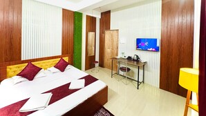 A hotel room with a bed, a desk, a television, and a ceiling fan. - B.B.Homestay & Guest House (Tezpur)