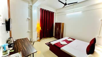 Quarto de hotel com cama, secretária com chaleira, luminária e armário.