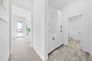 Un pasillo con una puerta que da a un baño y una zona de cocina con armarios.