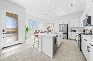 A modern kitchen with white cabinetry, a stainless steel refrigerator, and a large island with a sink. - 20% OFF Luxury 3BR Home, Modern Design & Comfort (Ontario)