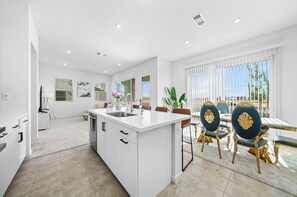 A modern kitchen with white cabinetry, a central island, and a dining area with a table and chairs. - 20% OFF Luxury 3BR Home, Modern Design & Comfort (Ontario)