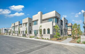 Un edificio residencial moderno de varios pisos con techo plano, ventanas grandes y un jardín frontal ajardinado.