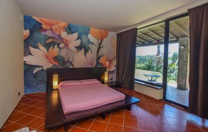 A bedroom with a bed, a large floral mural, a window with curtains, and a view of greenery outside. - Stunning home in Canale Monterano (Canale Monterano)