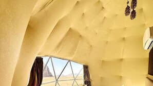 Una habitación con una cama, un sillón amarillo, una mesita y vistas al desierto a través de un ventanal grande.