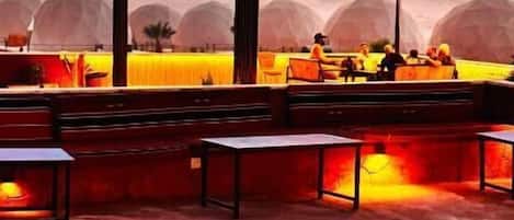 Un espace extérieur aménagé avec un foyer, des tables et une structure couverte.