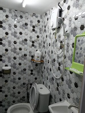 Casa de banho com padrão de azulejos hexagonais, sanita, bidé e uma estante verde.