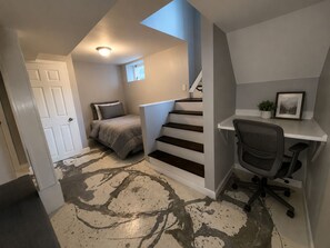 A bedroom with a bed, a desk, and a chair. There is a staircase leading to another level.