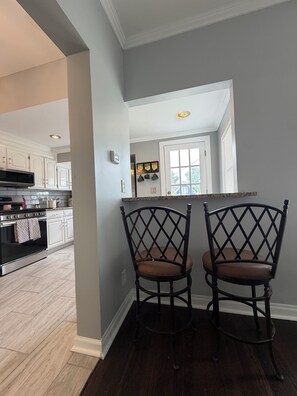 A kitchen with white cabinets, a microwave, and a stove. There are two chairs with a crisscross back design.