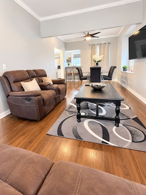 A modern living room with a brown leather sofa, a dining table with a black base, and a patterned rug.
