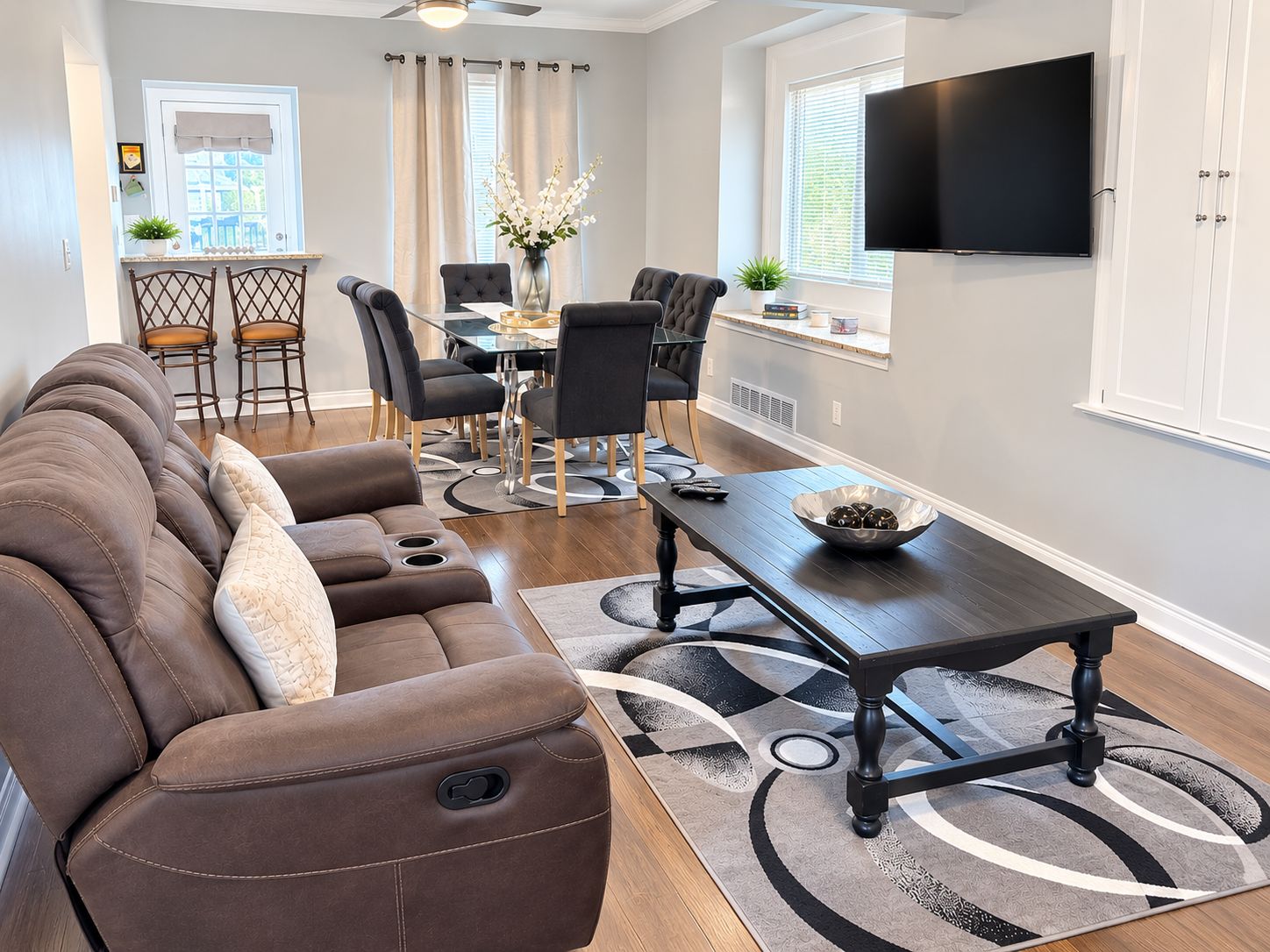 En moderne stue med sofa, spisebord, stole og et fladskærms-tv.