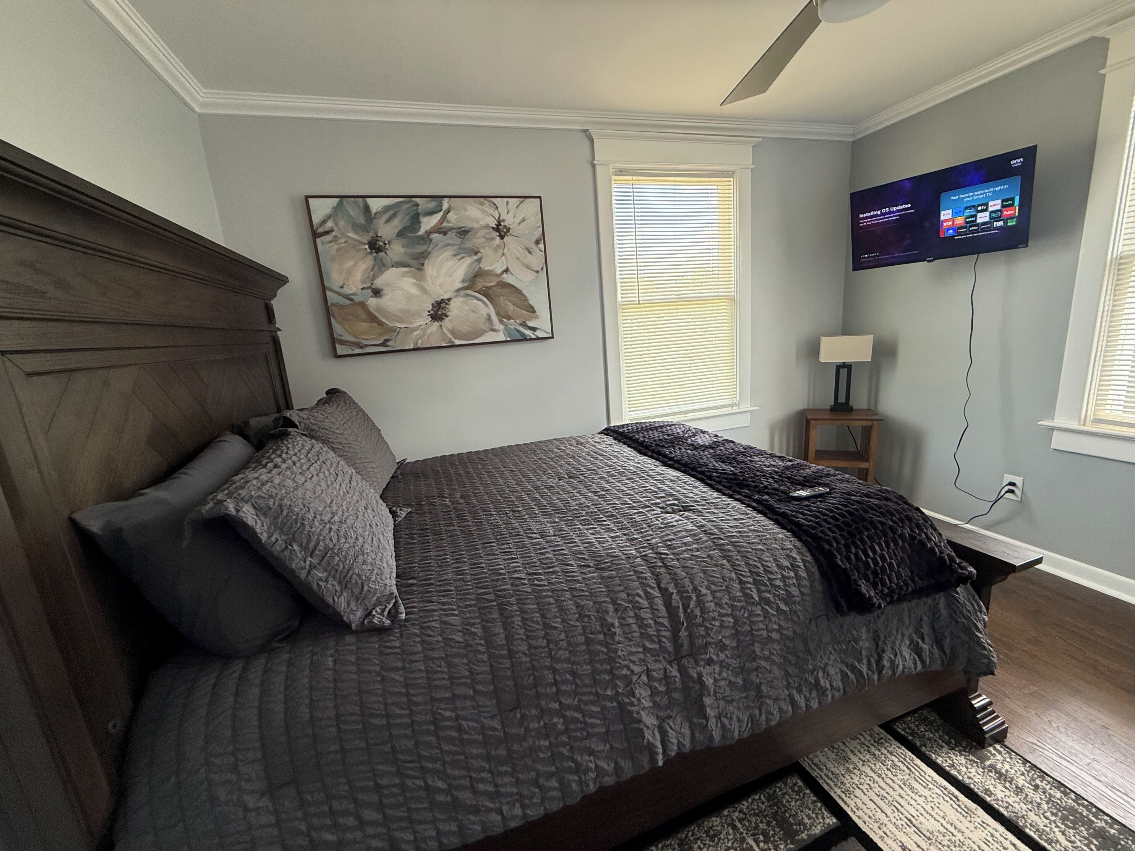 Une chambre à coucher avec un lit, un tableau, une télévision et une fenêtre avec des stores.