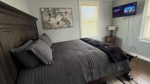 Una camera da letto con un letto, un quadro, una televisione e una finestra con persiane.