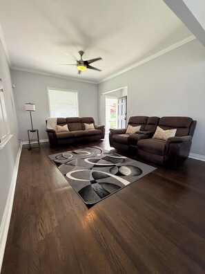 A living room with two brown sofas, a patterned rug, a standing lamp, and a ceiling fan.