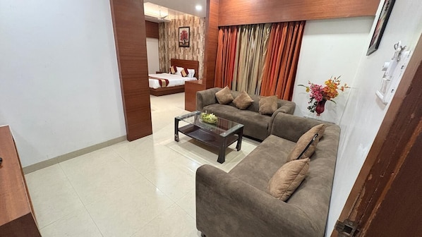 A living room with a sofa set, a coffee table, and a bed in the background.