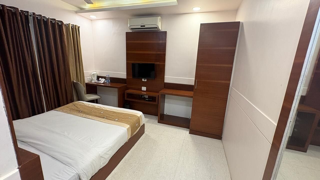 A hotel room with a bed, a desk with a chair, a television, and an air conditioning unit.