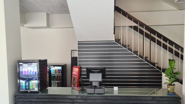 Un área de recepción con mostrador, máquina expendedora y una escalera que sube a plantas superiores.