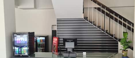 A reception area with a counter, a vending machine, and a staircase leading to upper floors.