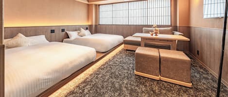 A hotel room with two beds, a small table, a sofa, and a large window.