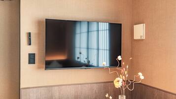 A flat-screen TV mounted on a wall with a wooden panel design, a remote control, and a thermostat on the wall.