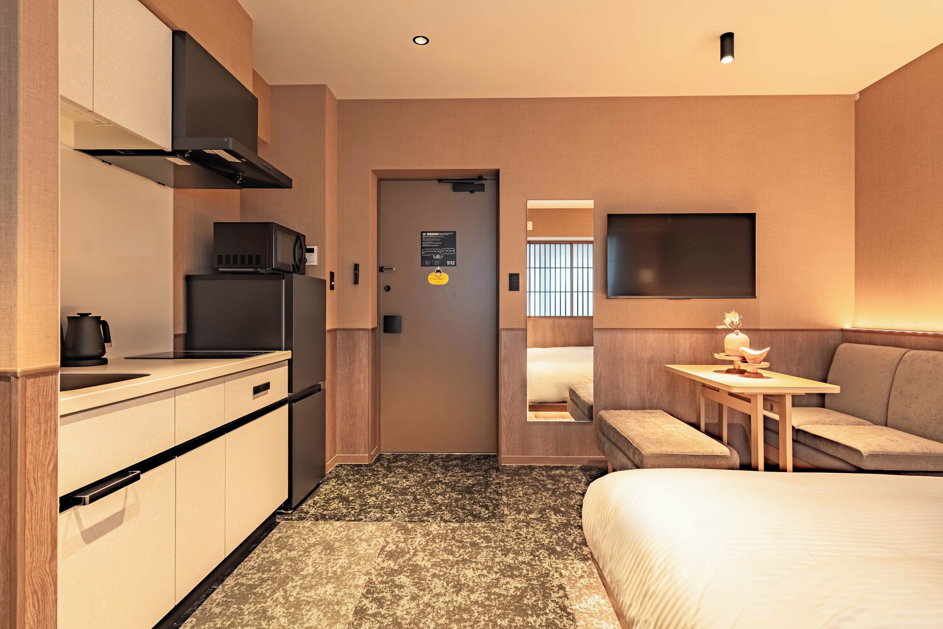 A hotel room with a kitchenette, a bed, a seating area, and a television.