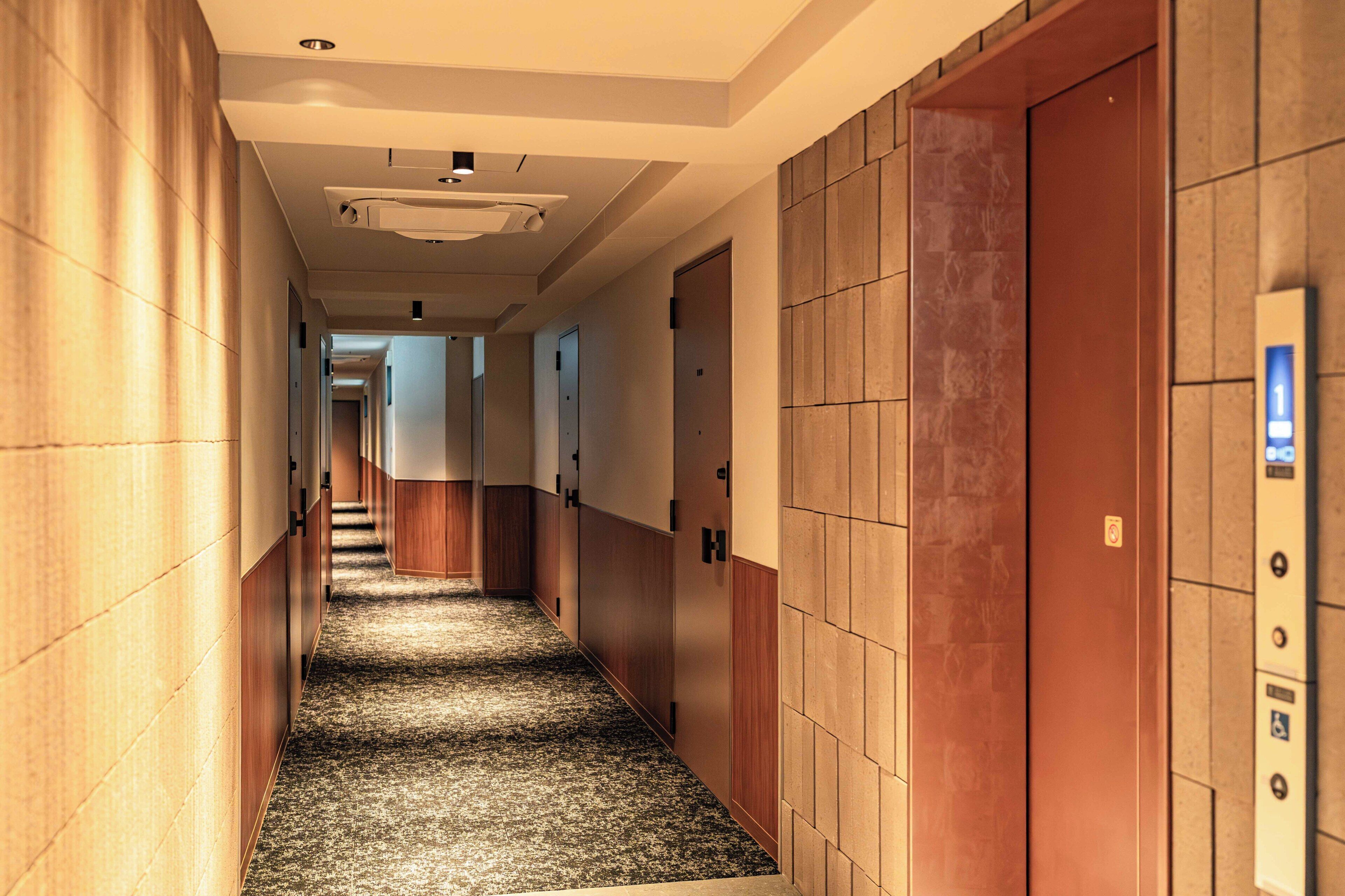 A hotel corridor with carpeted flooring, wooden panel walls, and doors leading to rooms.