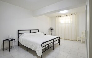 A bedroom with a bed, a bedside table, a fan, a chair, and a window with curtains. - Pet friendly home in Porto Empedocle with WiFi (Porto Empedocle)