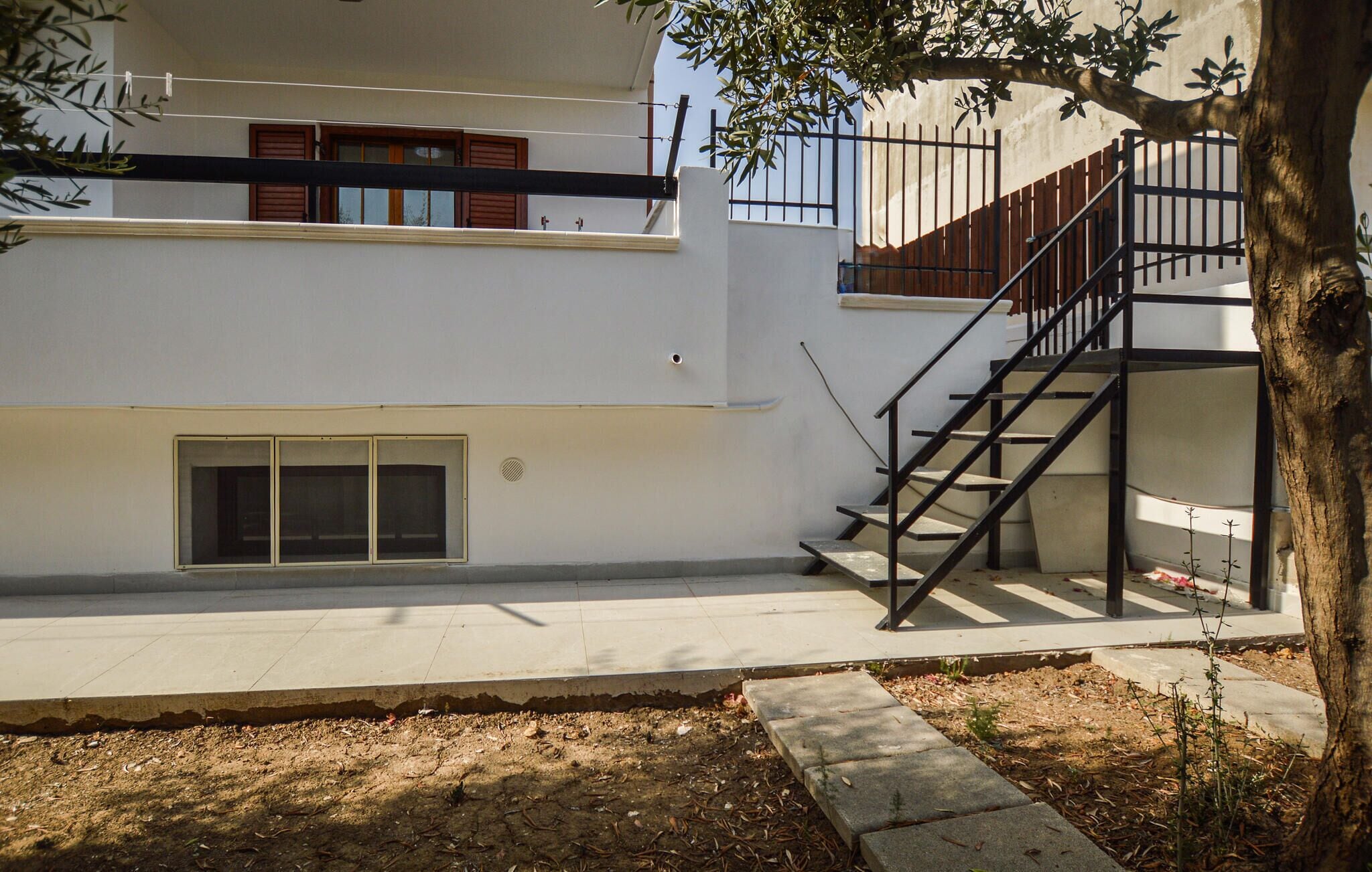 A modern building with a staircase leading to an upper level, a small window, and a tree in the foreground.